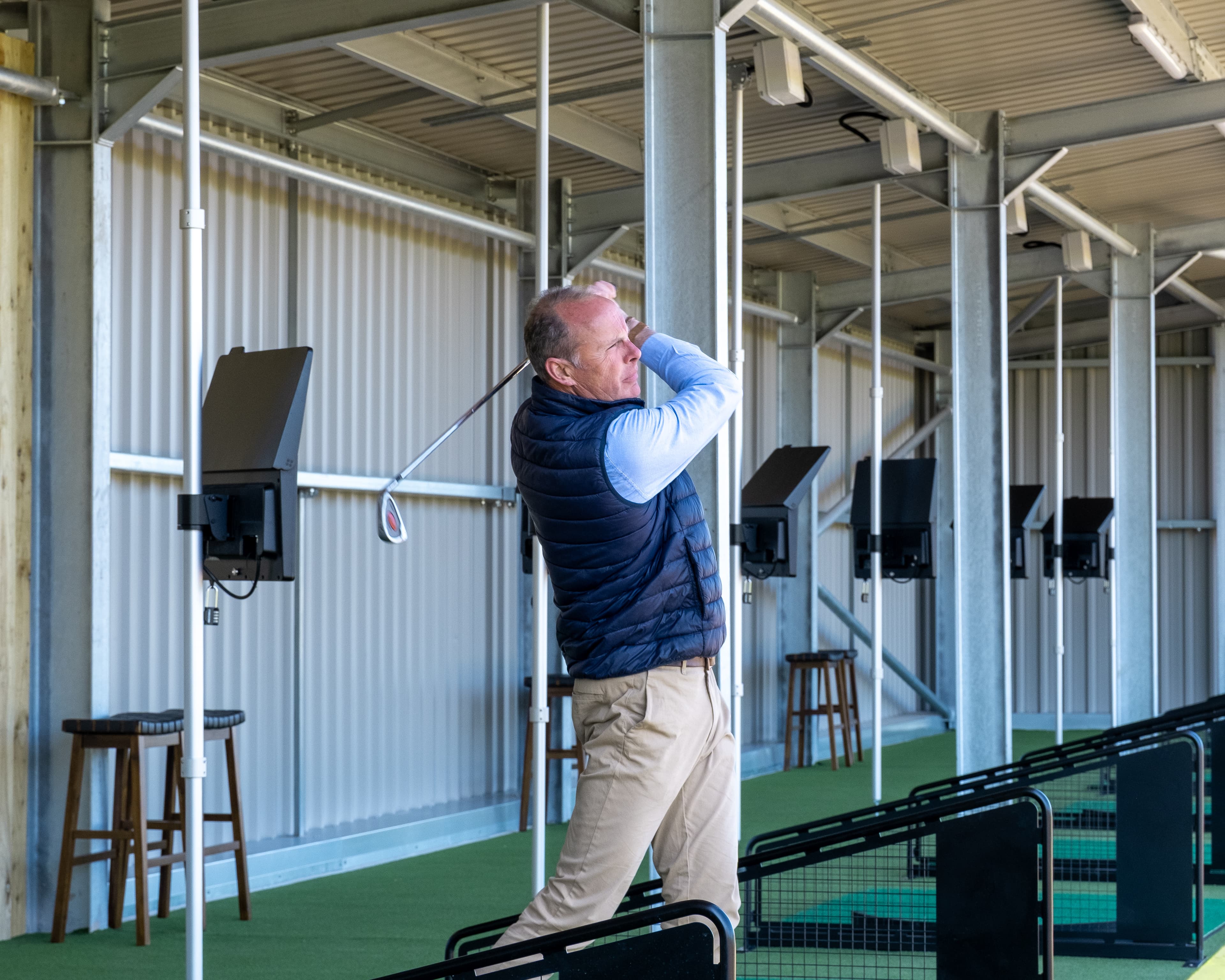 Robert Ashbrook on the follow-through at an Ashbrook Golf Zone covered Toptracer bay, the row of bays receding behind him