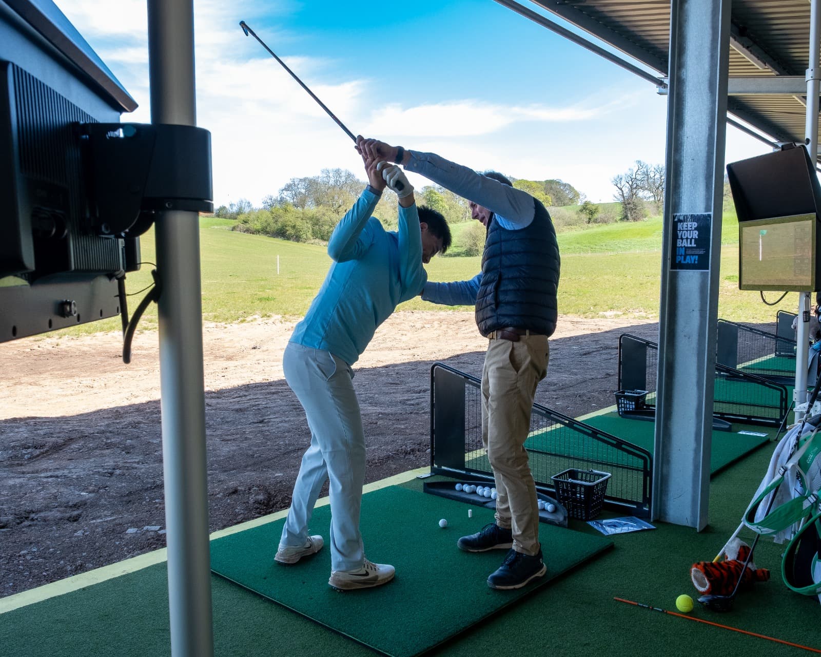 Robert Ashbrook, PGA Advanced Professional, guiding a student through the top of the backswing at an Ashbrook Golf Zone Toptracer bay — the practice field beyond
